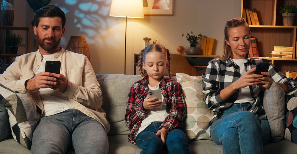 A family sits on a couch, each person focused on their own smartphone, illustrating screen time overuse and social disconnection.