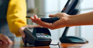 Shopper using a smartphone at a retail checkout with a contactless payment terminal